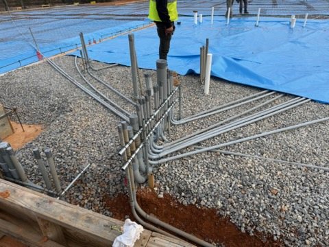 Rows of conduit with kicks, offsets, and stub-ups laid out on gravel before a slab pour.